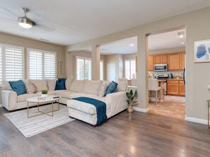 A spacious living room with a sectional sofa, a coffee table, and a dining area with wooden cabinets and a microwave. - Pools Golf and Tennis Home (Indio)