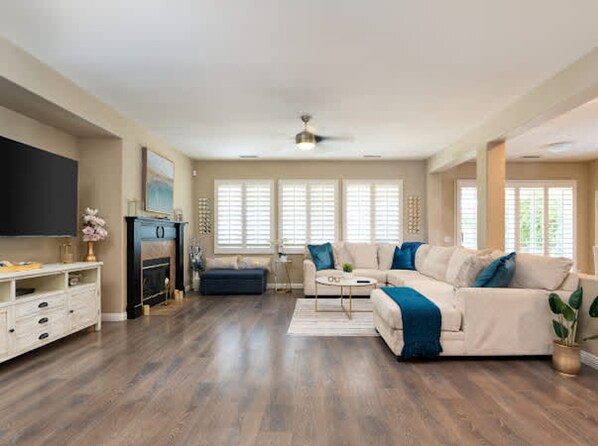 A spacious living room with a fireplace, a large sofa, and a television. - Pools Golf and Tennis Home (Indio)