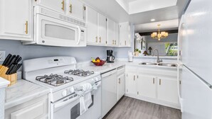 A modern kitchen with white cabinetry, a gas stove, a microwave, and a coffee maker. - South Cherokee in Palm Springs (Palm Springs)