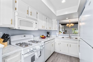 A modern kitchen with white cabinetry, a gas stove, a microwave, and a coffee maker. - South Cherokee in Palm Springs (Palm Springs)