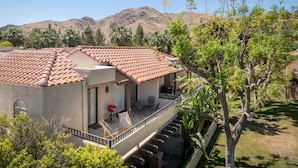 A two-story building with a red-tiled roof, a balcony with outdoor furniture, and a view of mountains in the background. - South Cherokee in Palm Springs (Palm Springs)
