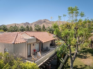 A two-story building with a red-tiled roof, a balcony with outdoor furniture, and a view of mountains in the background. - South Cherokee in Palm Springs (Palm Springs)