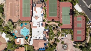 An aerial view of a residential area with multiple tennis courts, a swimming pool, and surrounding greenery. - South Cherokee in Palm Springs (Palm Springs)