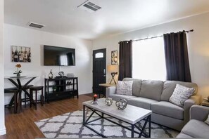A modern living room with a grey sofa, a coffee table, a TV, and a dining area with a table and chairs. - Central Location One Bedroom Apartment Parking (North Hollywood)