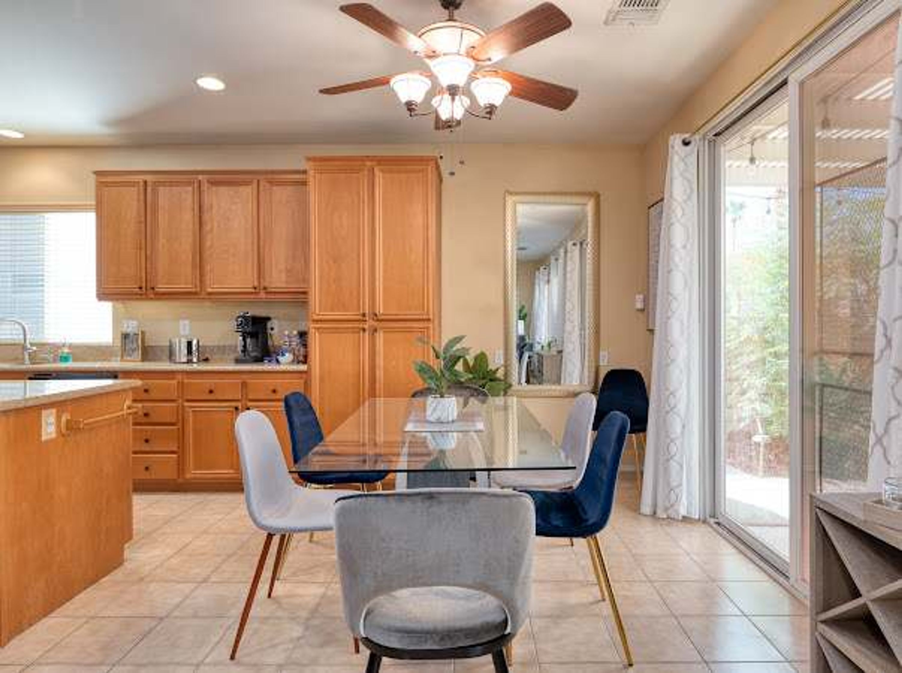 A kitchen with wooden cabinets, a dining table with chairs, a ceiling fan, and a window with a view.