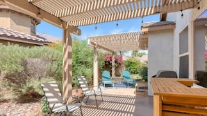 Un patio cubierto con un pérgola, asientos exteriores y una mesa.