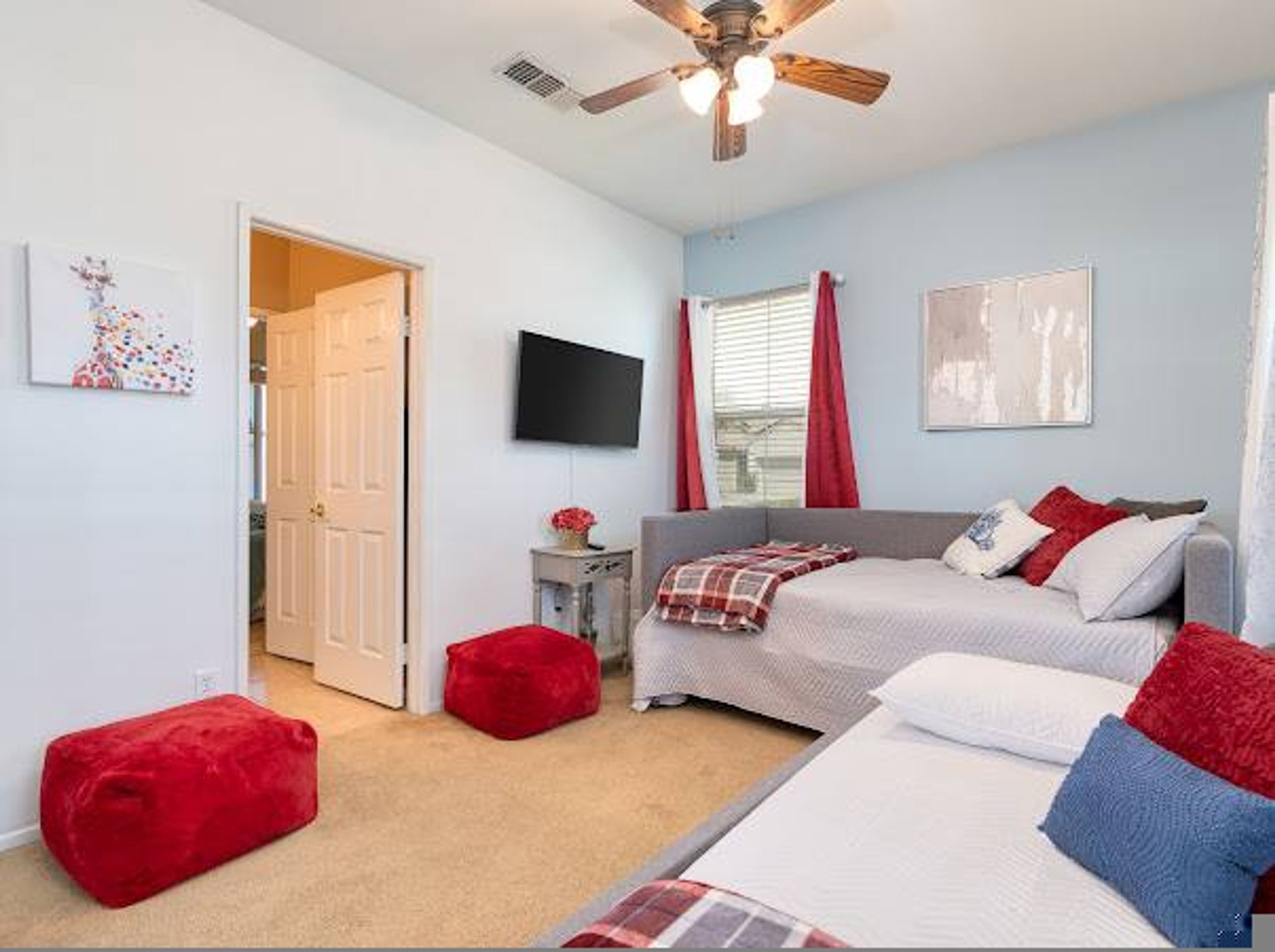 A bedroom with two beds, a ceiling fan, a TV, and a door leading to another room.