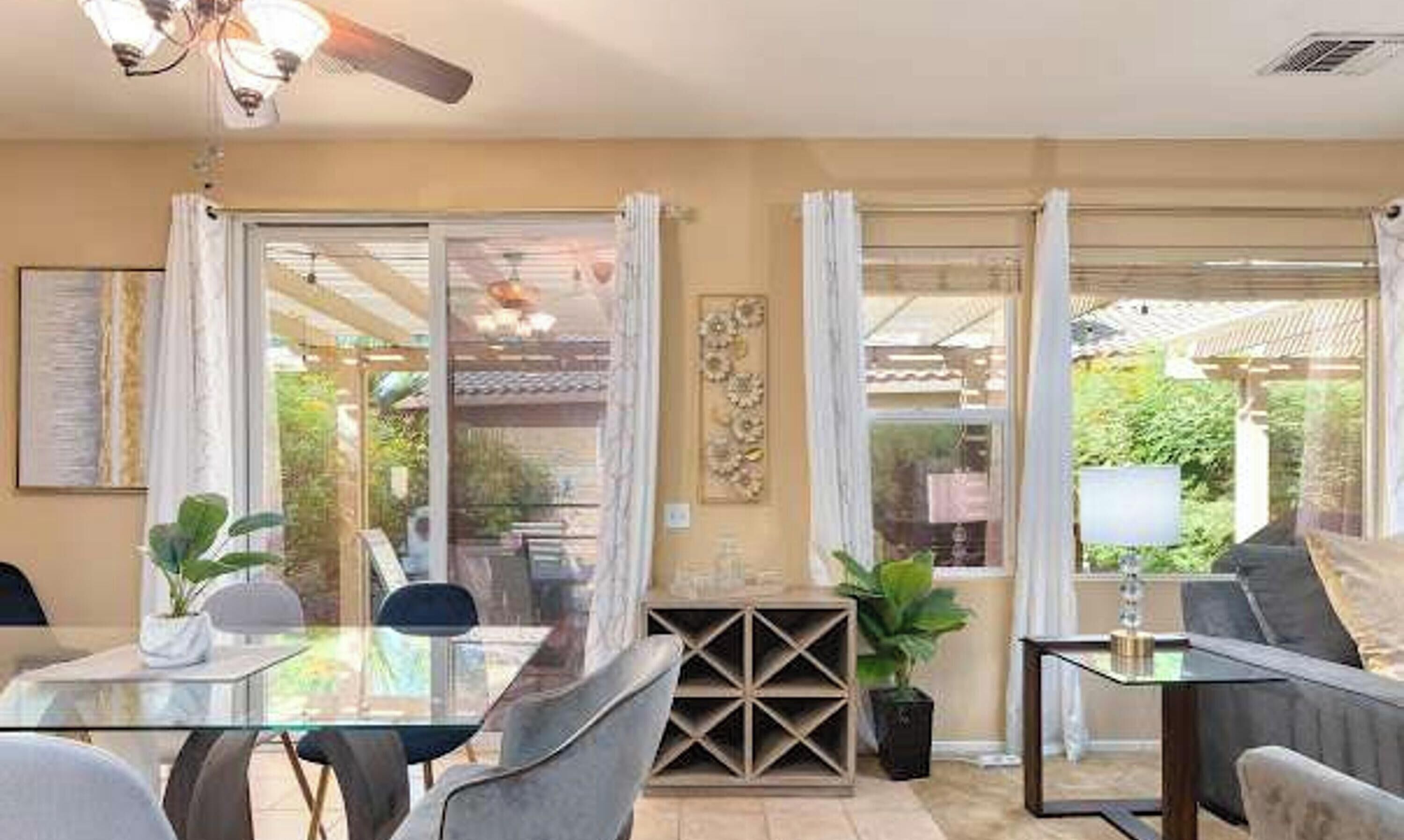 Un comedor con una mesa de vidrio, sillas, un ventilador de techo y vistas al exterior.