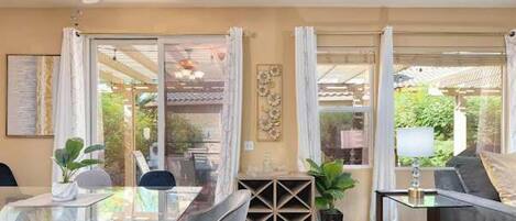 Un comedor con una mesa de vidrio, sillas, un ventilador de techo y vistas al exterior.