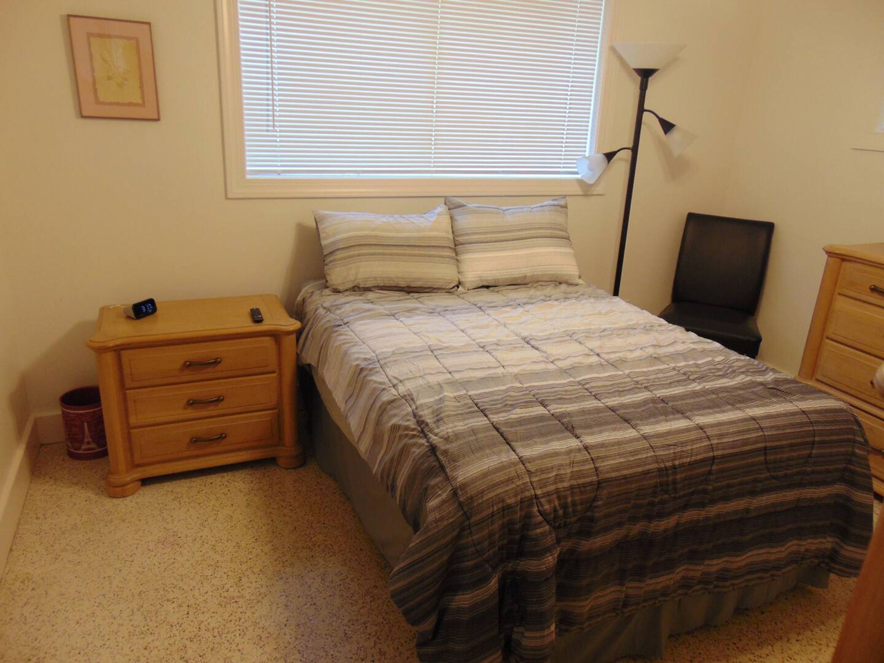 Een slaapkamer met een bed, nachtkastje, lamp en een dressoir.