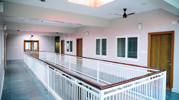 A spacious corridor with a wooden railing, multiple doors, and ceiling fans. - Aldur Residency (Chikkamagaluru)
