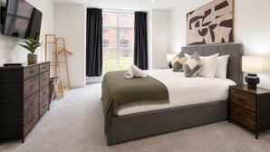 A bedroom with a bed, a TV, a dresser, a bedside table, and a window with curtains. - Modern 1BR - Sleeps 4 - Free Parking - Manchester (Manchester)