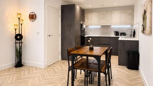 A modern kitchen with grey cabinets, a wooden dining table with chairs, and a small side table with a vase. - Modern 1BR - Sleeps 4 - Free Parking - Manchester (Manchester)