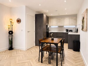 A modern kitchen with grey cabinets, a wooden dining table with chairs, and a small side table with a vase. - Modern 1BR - Sleeps 4 - Free Parking - Manchester (Manchester)