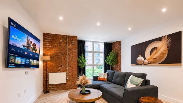 A modern living room with a flat-screen TV, a sofa, a coffee table, and a decorative wall piece. - Modern 1BR - Sleeps 4 - Free Parking - Manchester (Manchester)