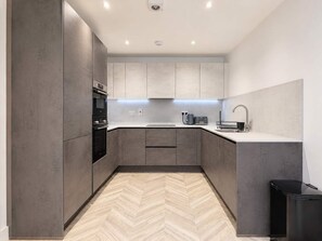 A modern kitchen with grey cabinetry, a herringbone-patterned floor, a built-in oven, and a sink with a modern faucet. - Modern 1BR - Sleeps 4 - Free Parking - Manchester (Manchester)