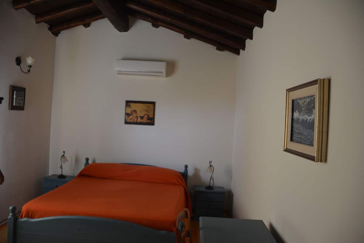 A bedroom with a bed, two bedside tables, an air conditioner, and two wall-mounted lamps.