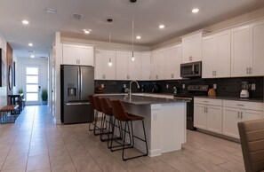 Una cocina moderna con armarios blancos, electrodomésticos de acero inoxidable y una isla central con taburetes de bar.