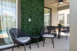 Een balkon met twee rieten stoelen, een klein tafeltje en een groene wand.