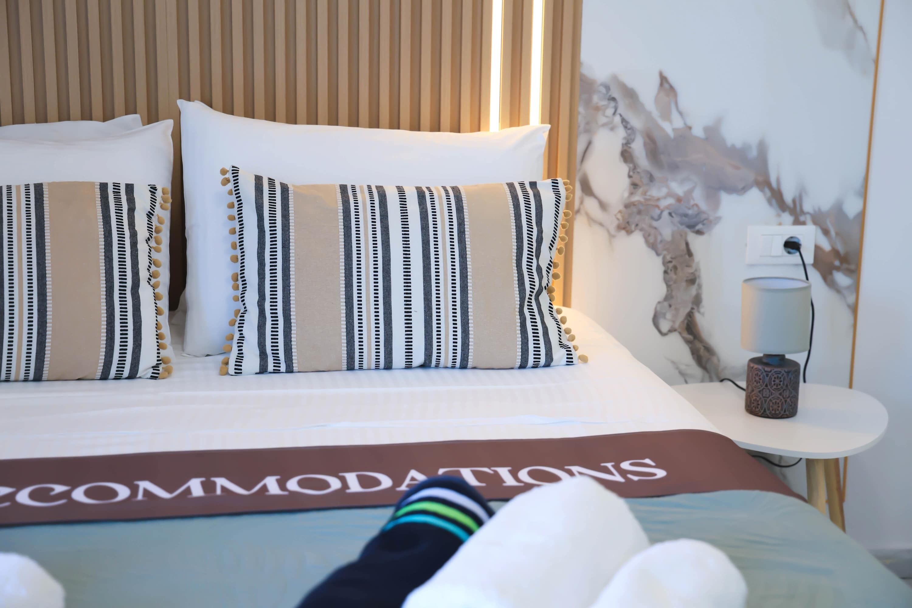 A hotel room with a bed, pillows, a bedside table, and a wall with a textured design.