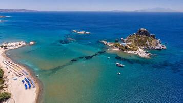 Vista aérea de uma área costeira com praia, águas azul-claras e afloramentos rochosos.