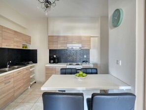 Eine moderne Küche mit Holzausstattung, einer weißen Arbeitsplatte, einem Herd und einem Spülbecken. Ein Esstisch mit Stühlen und eine Schüssel mit Obst sind ebenfalls vorhanden.
