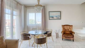 Uma área de refeições com uma mesa de vidro redonda, quatro cadeiras, um candelabro, um sofá e uma poltrona grande.