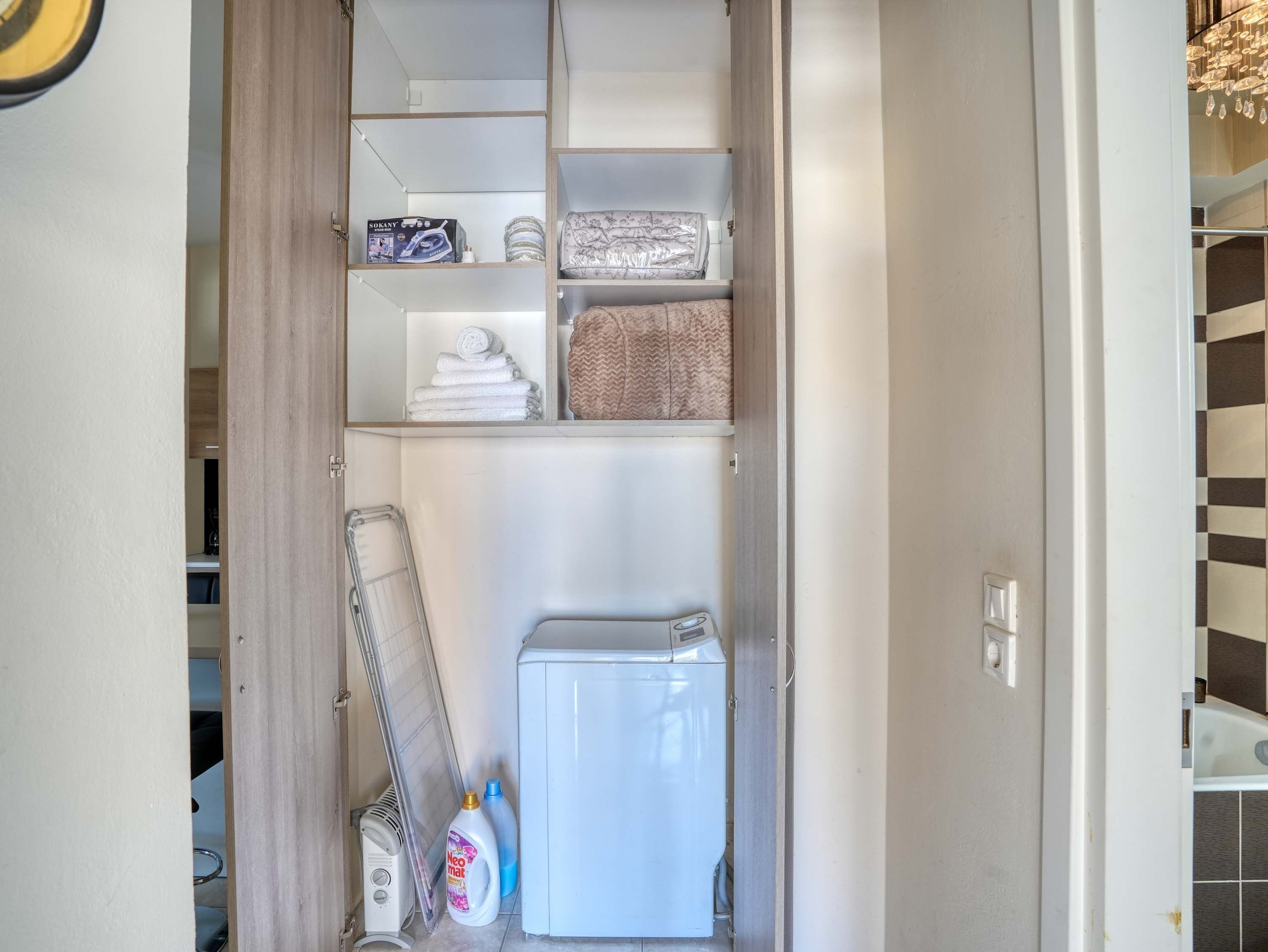 A compact storage area with shelves, a drying rack, and a small white appliance, likely a mini-fridge or heater.