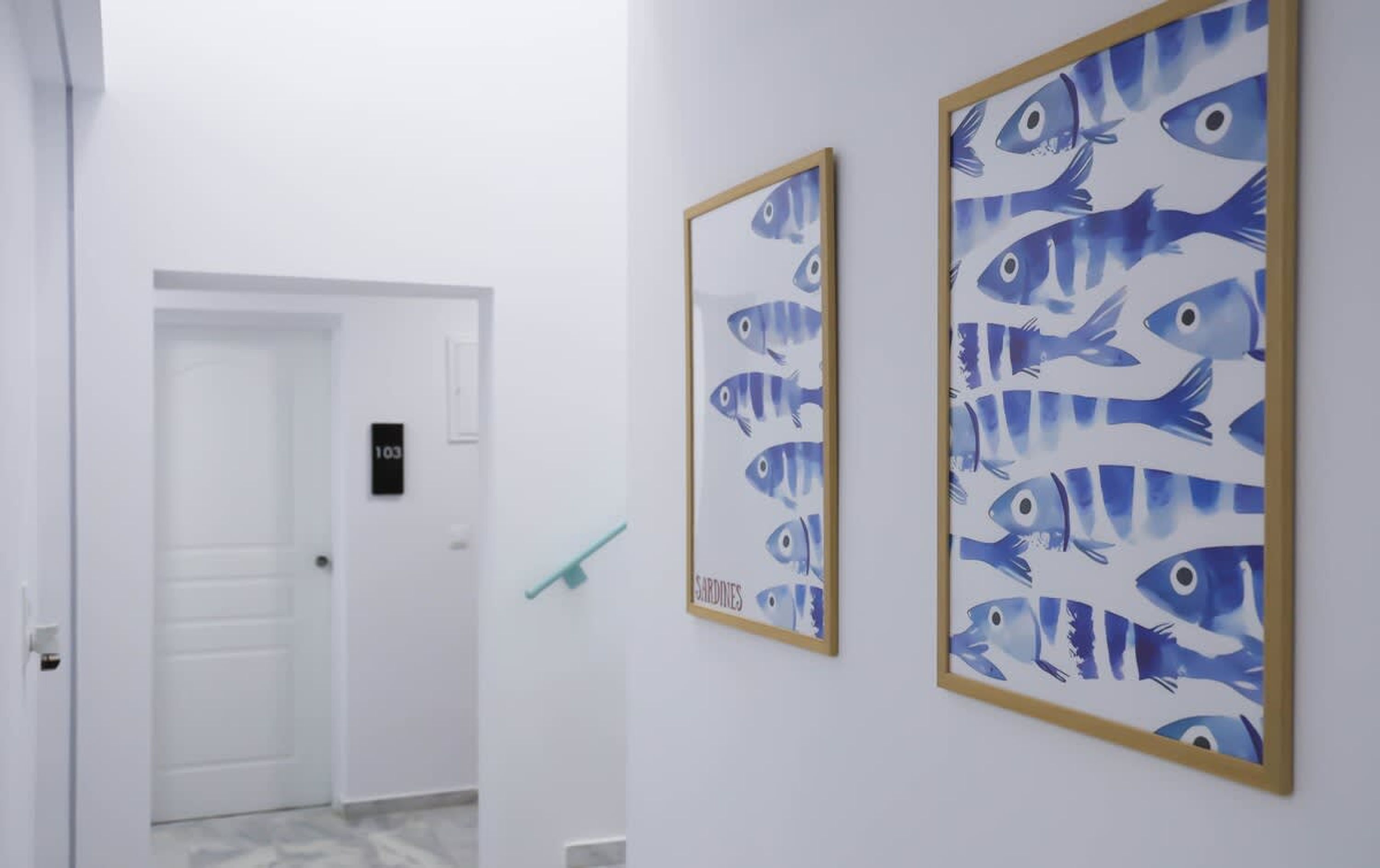 A hallway with two framed fish paintings on the wall, a door with a number sign, and a green object on the floor.