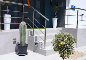 Ein moderner Gebäudeeingang mit Metalltreppe, Pflanzkübeln und einem Schild.