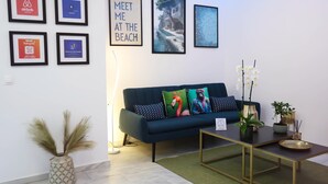 Una sala moderna con un sofá azul oscuro, cuadros en la pared, un jarrón con plumas de pampa y una mesita con una bandeja.