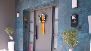 Entrada de edificio con puerta, un cartel con número, una corona y dos macetas.