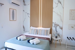 Ein Hotelzimmer mit Bett, Nachttisch, Wandklimaanlage und einem gerahmten Bild an der Wand.