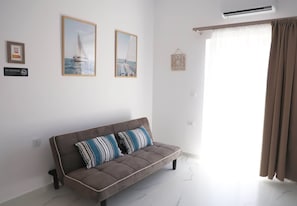 Ein modernes Wohnzimmer mit einer Couch, zwei gerahmten Bildern, einem Rauchverbot-Schild und einem Fenster mit Vorhängen.