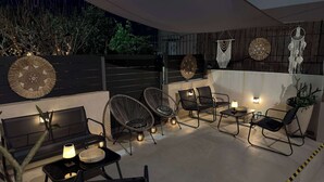 An outdoor seating area with chairs and tables, decorative wall art, and ambient lighting. - Apartment Simply 205 - Ammoudara Sandy Retreat (Malevizi)