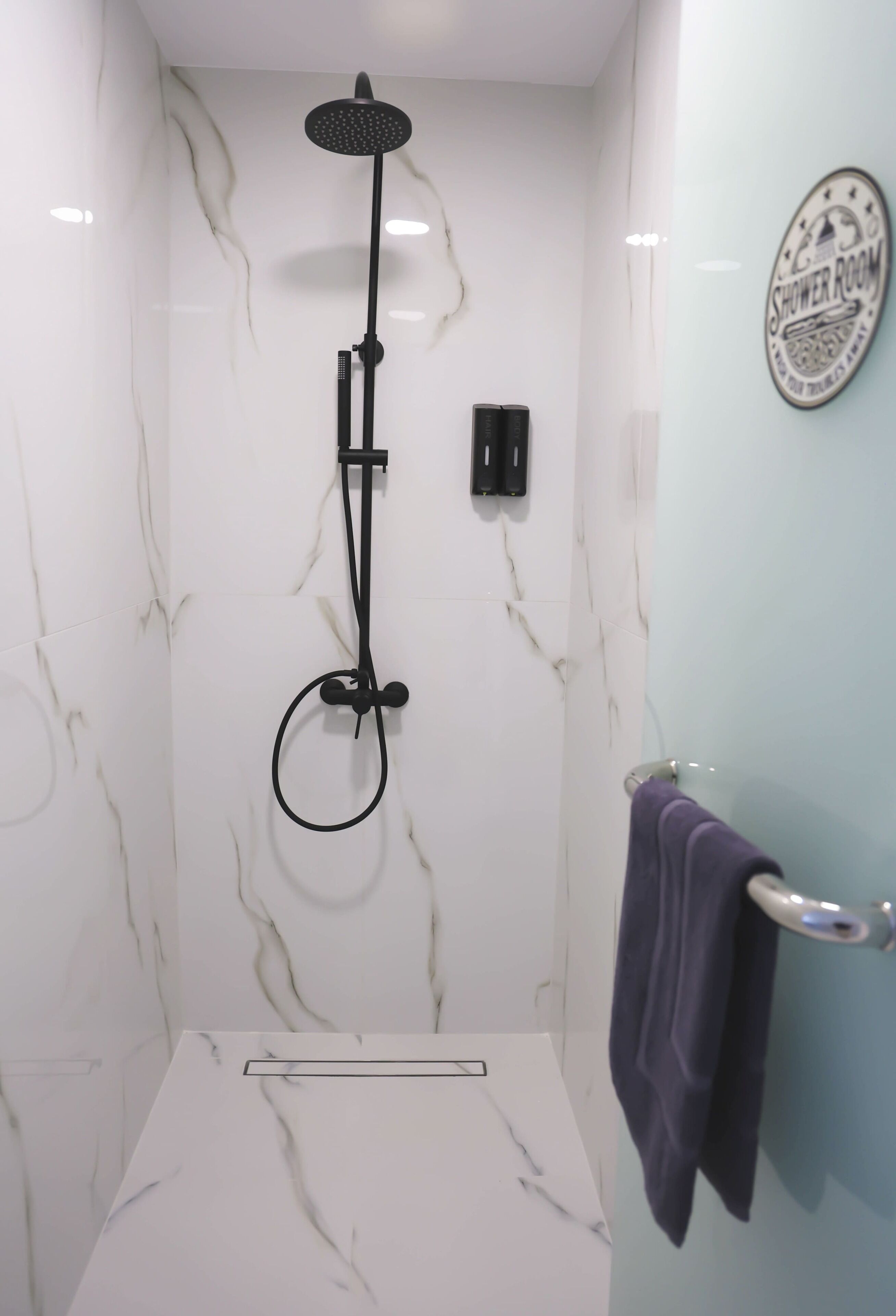Une douche équipée d’un pommeau de douche à main et d’un panneau de commande fixé au mur.