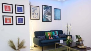 A modern living room with a dark blue sofa, framed pictures on the wall, and a small table with a vase of flowers. - Apartment Simply 205 - Ammoudara Sandy Retreat (Malevizi)