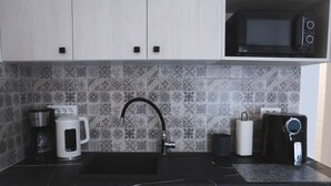 A kitchen with a black countertop, a coffee maker, a kettle, a microwave, and a sink with a modern faucet. - Apartment Simply 205 - Ammoudara Sandy Retreat (Malevizi)