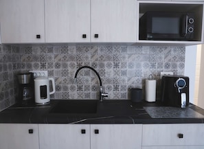 Eine Küche mit schwarzem Arbeitsplatz, einer Kaffeemaschine, einem Wasserkocher, einer Mikrowelle und einem Spülbecken mit modernem Wasserhahn.