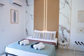 Ein Hotelzimmer mit Bett, einem kleinen Tisch, einem Sessel und einer Wand mit Kunstwerken.