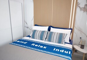 Ein Bett mit einer blau-weißen Tagesdecke, zwei Kissen und einem gestreiften Kopfkissen.