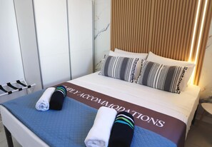 Une chambre d’hôtel avec un lit, des oreillers, une serviette et une pancarte indiquant « HÉBERGEMENT ».