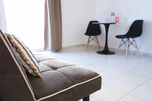 Ein modernes Zimmer mit einer Couch, zwei schwarzen Stühlen, einem kleinen Tisch mit Gegenständen und einem Fenster mit Vorhängen.