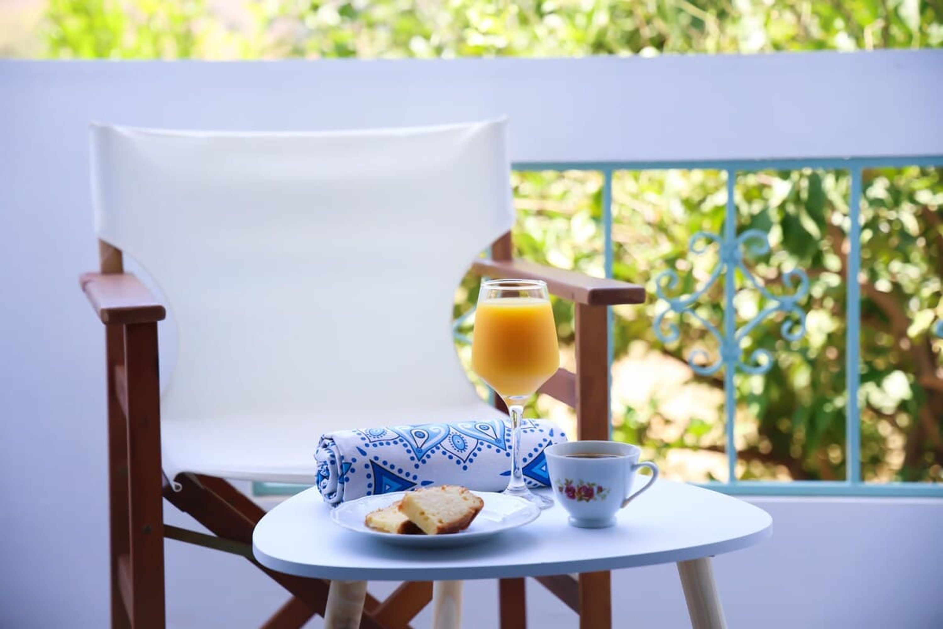 A white chair, a small round table with a cup, a glass of orange juice, and a plate with a slice of bread.