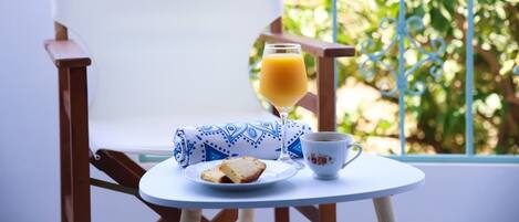 A white chair, a small round table with a cup, a glass of orange juice, and a plate with a slice of bread.