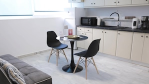 A modern kitchen with a dining area, including a sofa, two chairs, a round table, and a microwave. - Apartment Simply 101 - Ammoudara Sandy Retreat (Malevizi)