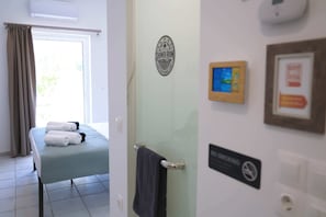 Ein Hotelzimmer mit Massagetisch, Handtuchhalter, einem Nichtraucher-Schild und einem an der Wand befestigten digitalen Bildschirm.