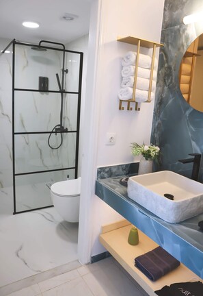 Ein modernes Badezimmer mit einer Glasdusche, einer weißen Toilette, einem Marmorboden, einem Marmorwaschbecken und einem Handtuchhalter mit gefalteten Handtüchern.