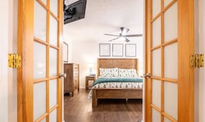 Ein Zimmer mit einem Bett, einem Deckenventilator, einem Schminktisch und gerahmten Bildern an der Wand.