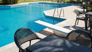 A swimming pool with lounge chairs and a table, surrounded by greenery and buildings.